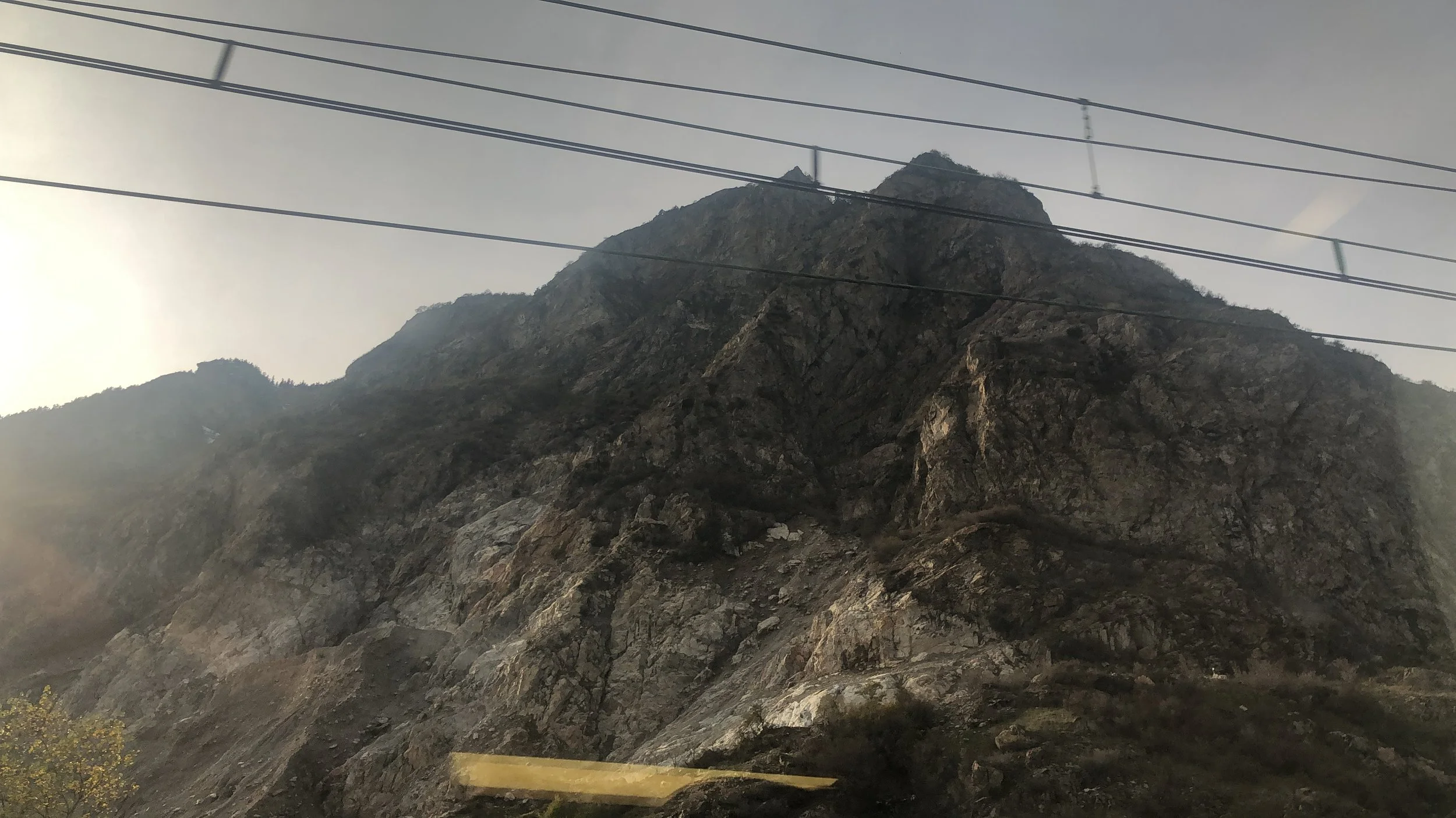 Montagna rocciosa sotto un cielo chiaro con cavi elettrici.