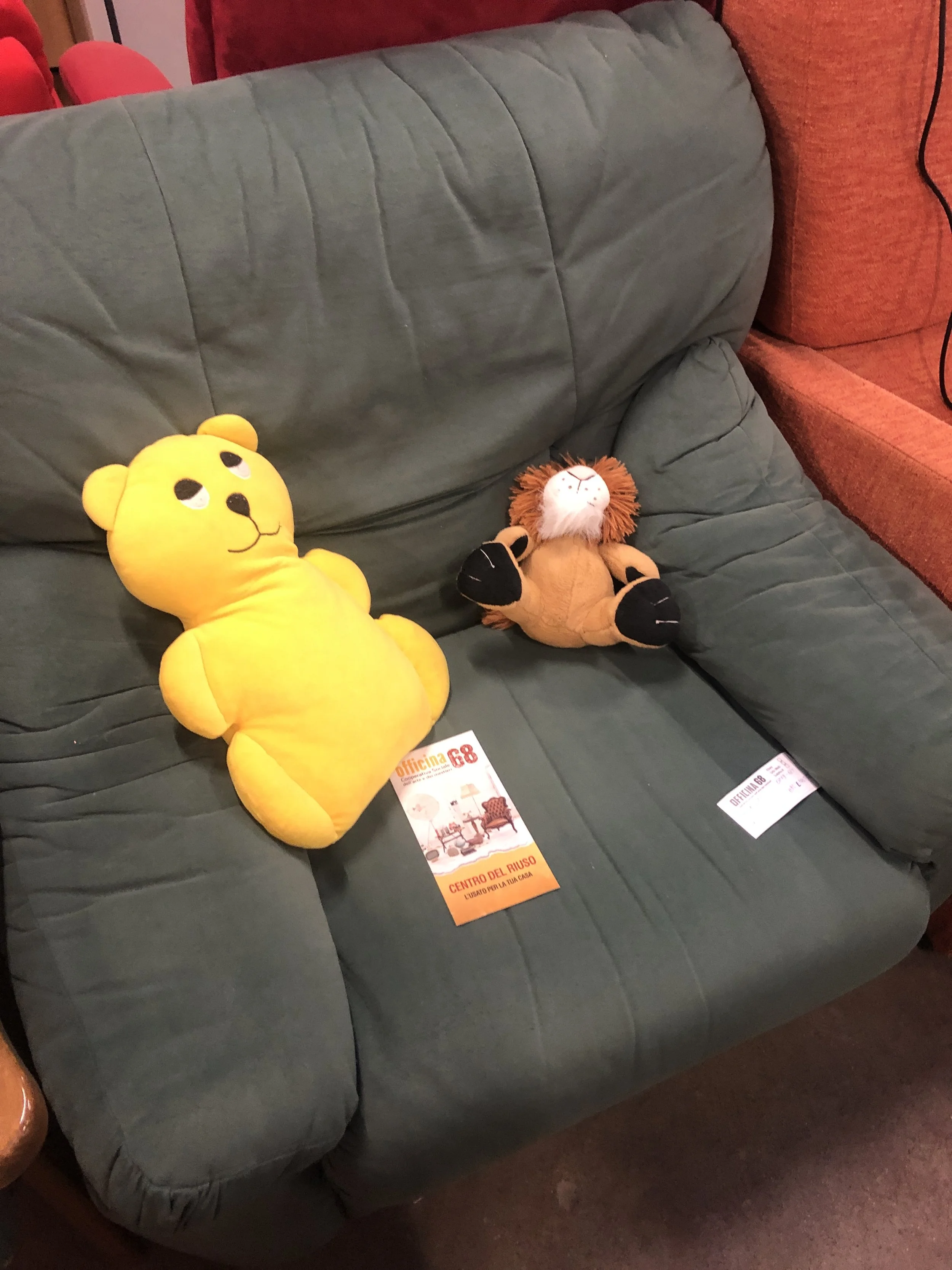 Due peluche, un orsacchiotto giallo e un leone, su una poltrona verde, con un opuscolo sul sedile.