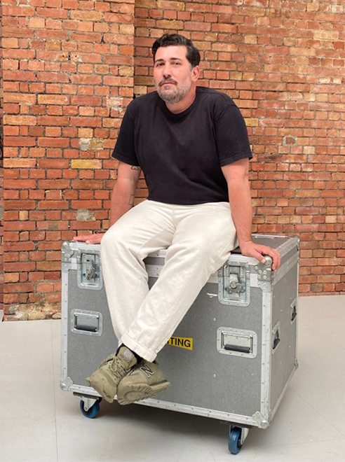 A man sitting on a large gray equipment case with a brick wall background.