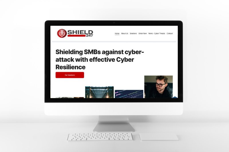 A computer monitor displaying a website titled 'Shield 247' with a slogan about shielding SMBs against cyberattacks and a red 'Our Solutions' button, set against a light background.