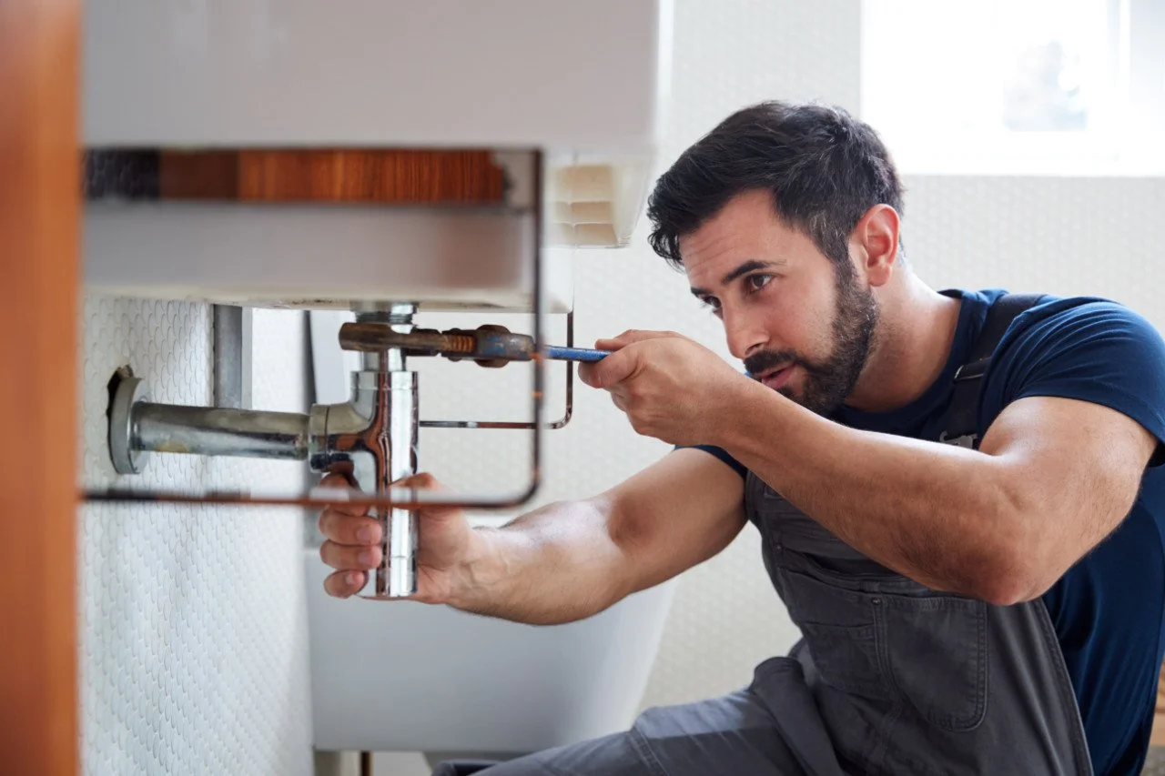 A plumber fixing a sink pipe underneath a bathroom sink with a wrench.