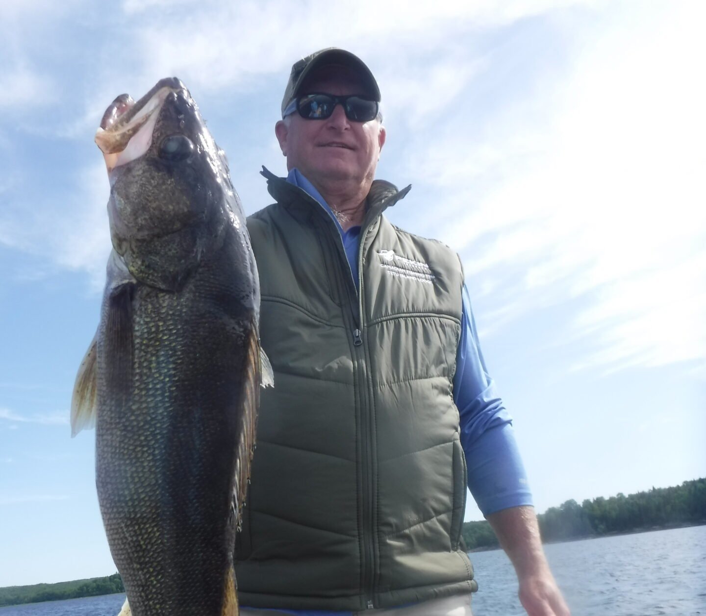 Person holding a large fish on a boat with water and sky in the background.
