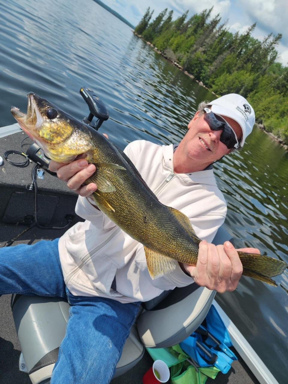 Person holding a fish on a boat with a lake and forest background.