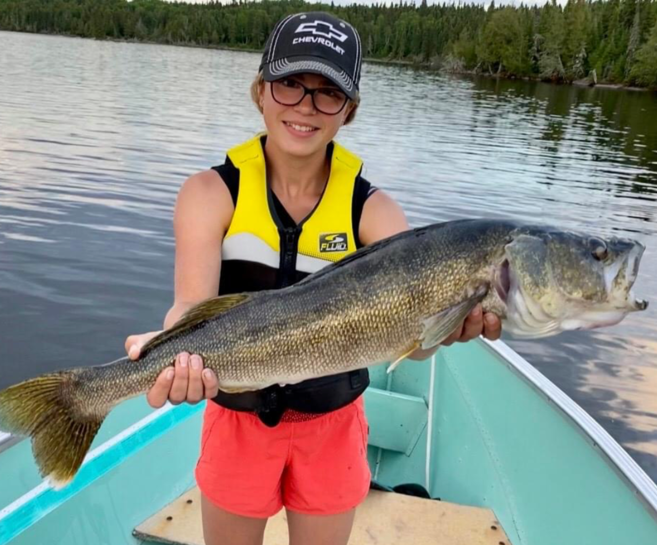 Person holding a large fish on a boat in a lake.