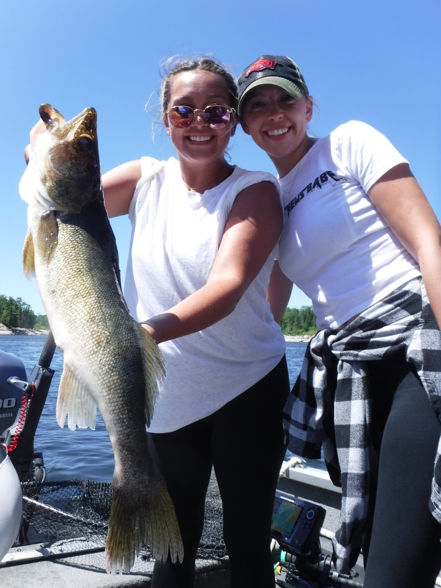 Two people holding a large fish on a boat with a lake in the background.
