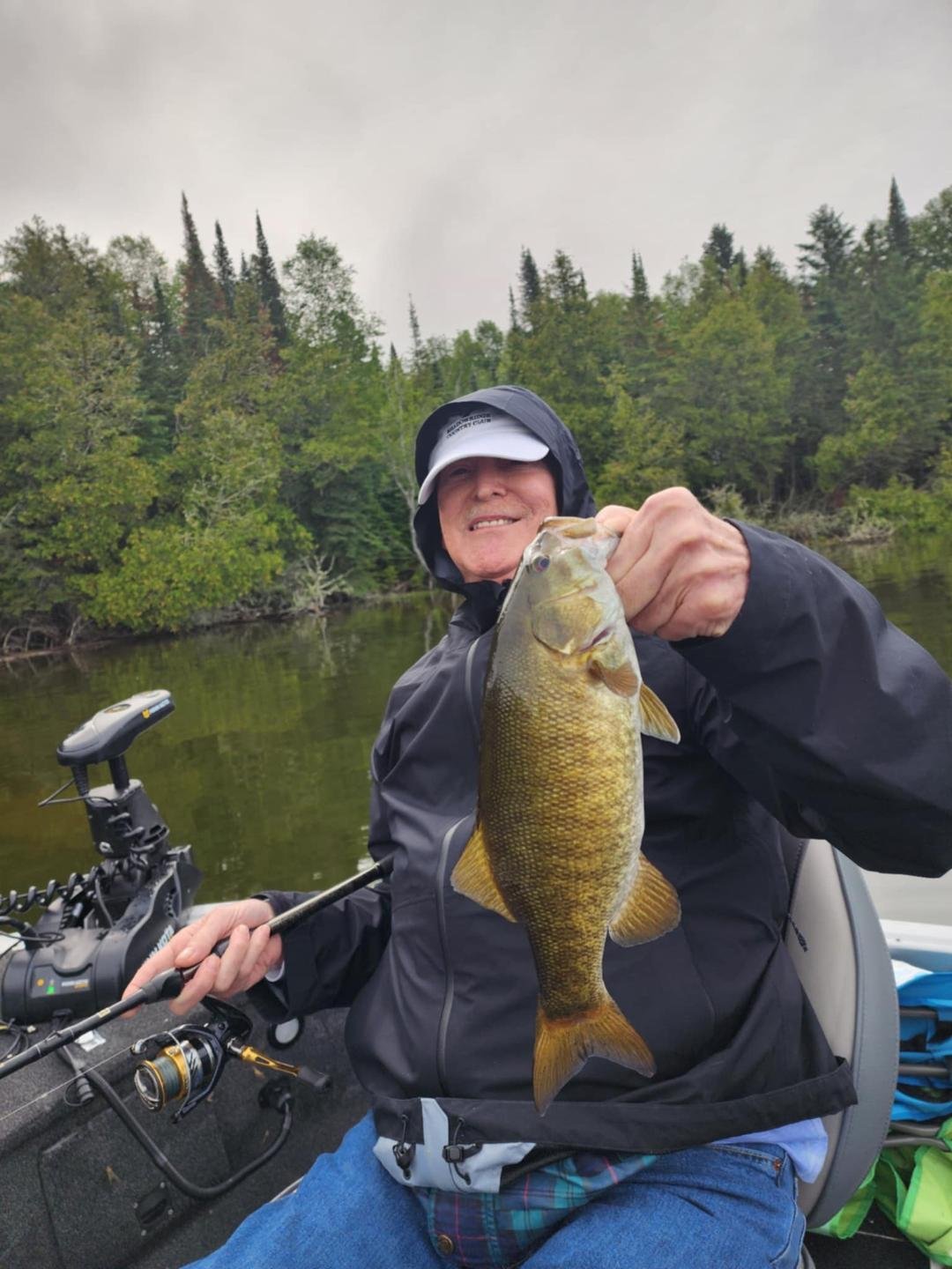 Person holding a fish in a boat on a lake with trees in the background.