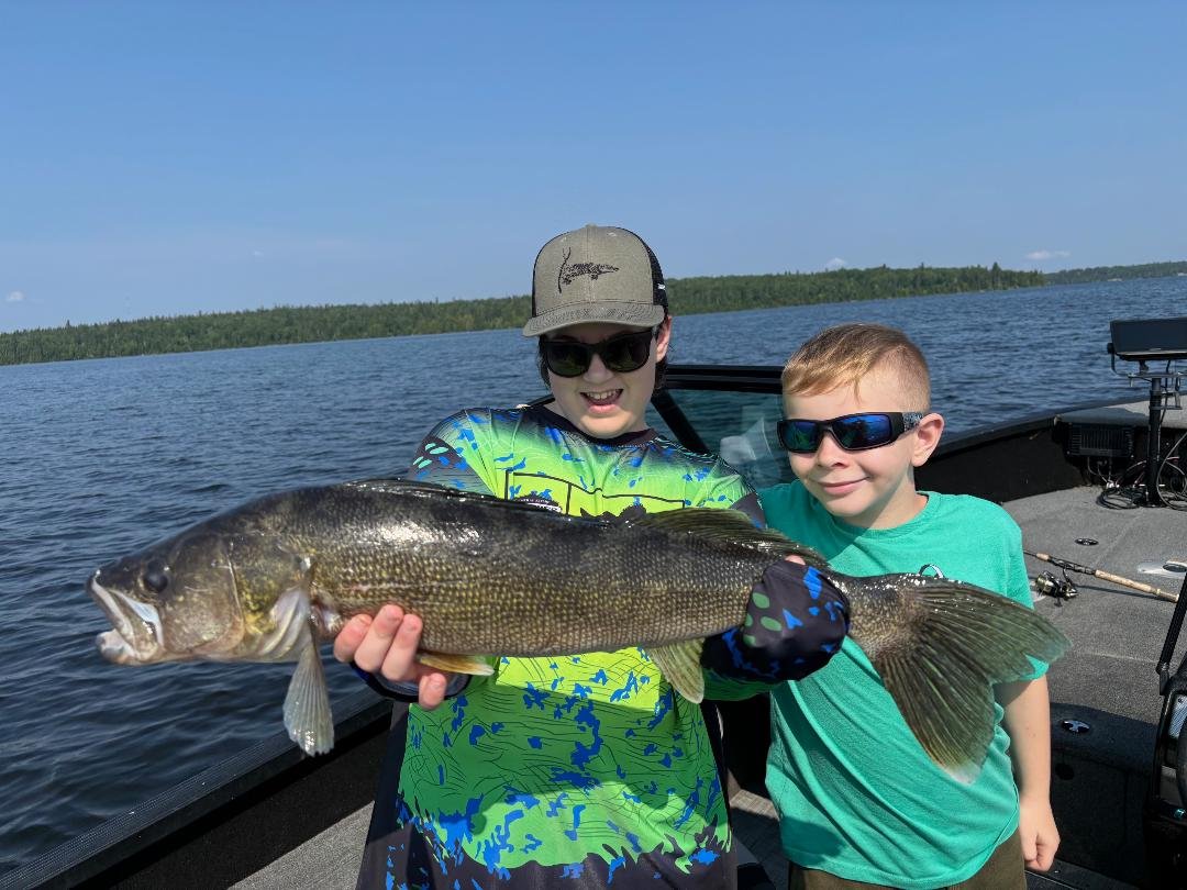 Two kids holding a large fish on a boat in a lake.