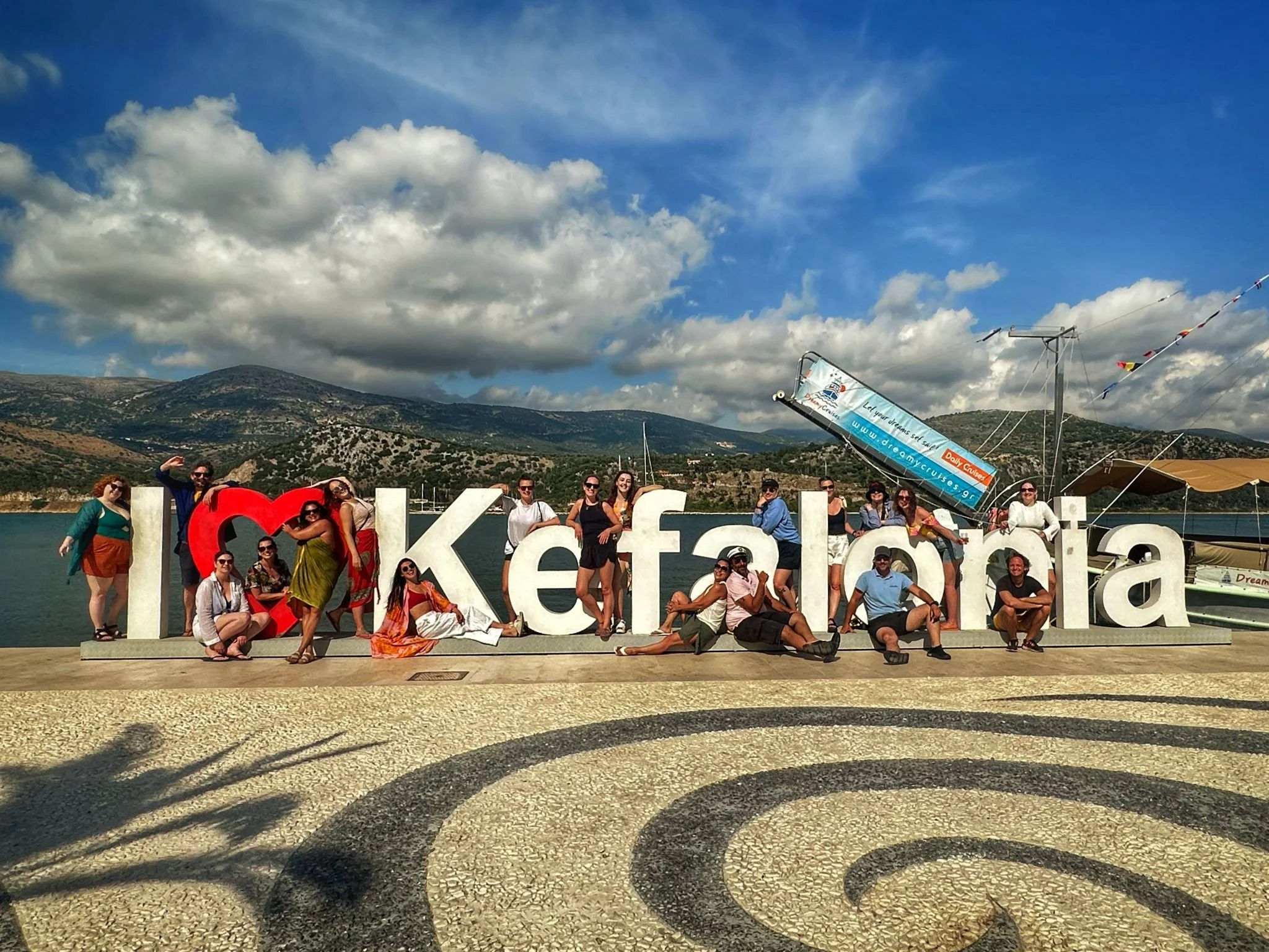 A photo of a sign which says 'I love Kefalonia' with past retreat guests standing and smiling in between the letters