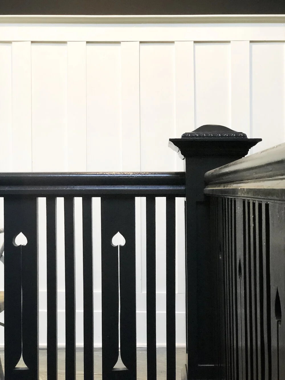 Close-up of a black wooden staircase railing with decorative cutouts, against a white paneled wall.