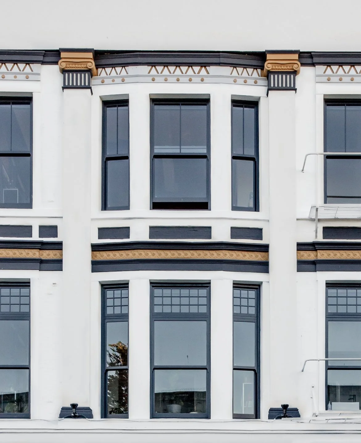 Front view of a multi-story building with white exterior walls, black window frames, and decorative brown and black trim at the top.