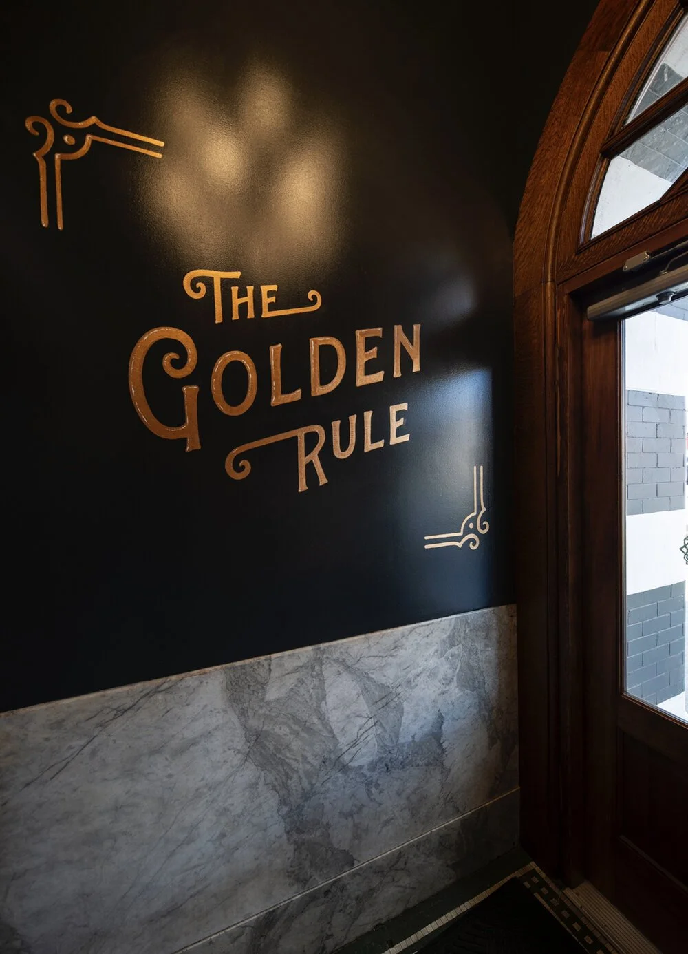 Decorative wall sign reading 'The Golden Rule' in a restaurant or cafe, with wooden and marble accents and a door nearby.
