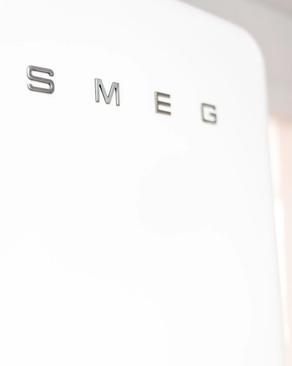 Close-up of the word 'SMEG' in silver letters on a white surface, likely a refrigerator door.