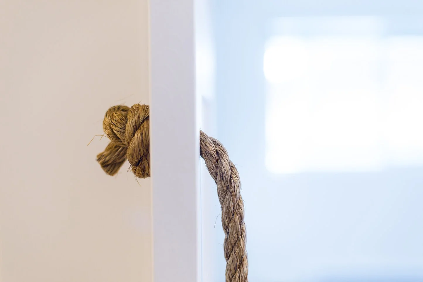 Close-up of a door with a rope tied around the door handle, featuring a knotted and frayed end.