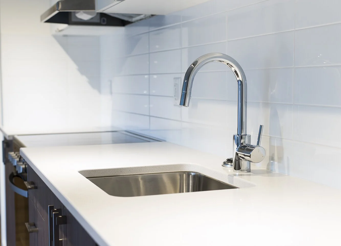 Modern kitchen sink with a chrome faucet and white countertop, against a light blue tiled wall.