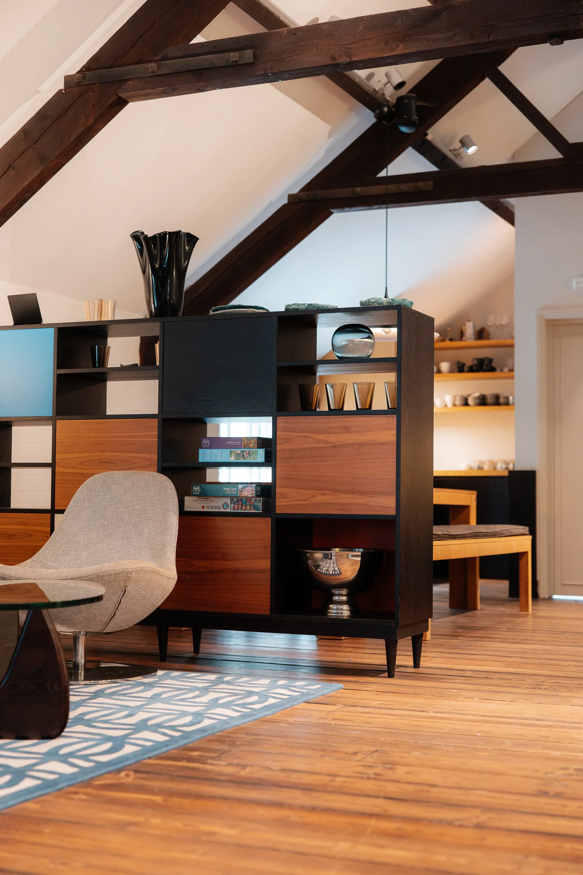 Interior view of a living room with wooden floors, a modern multicolored shelving unit, a beige armchair, and a blue patterned rug.