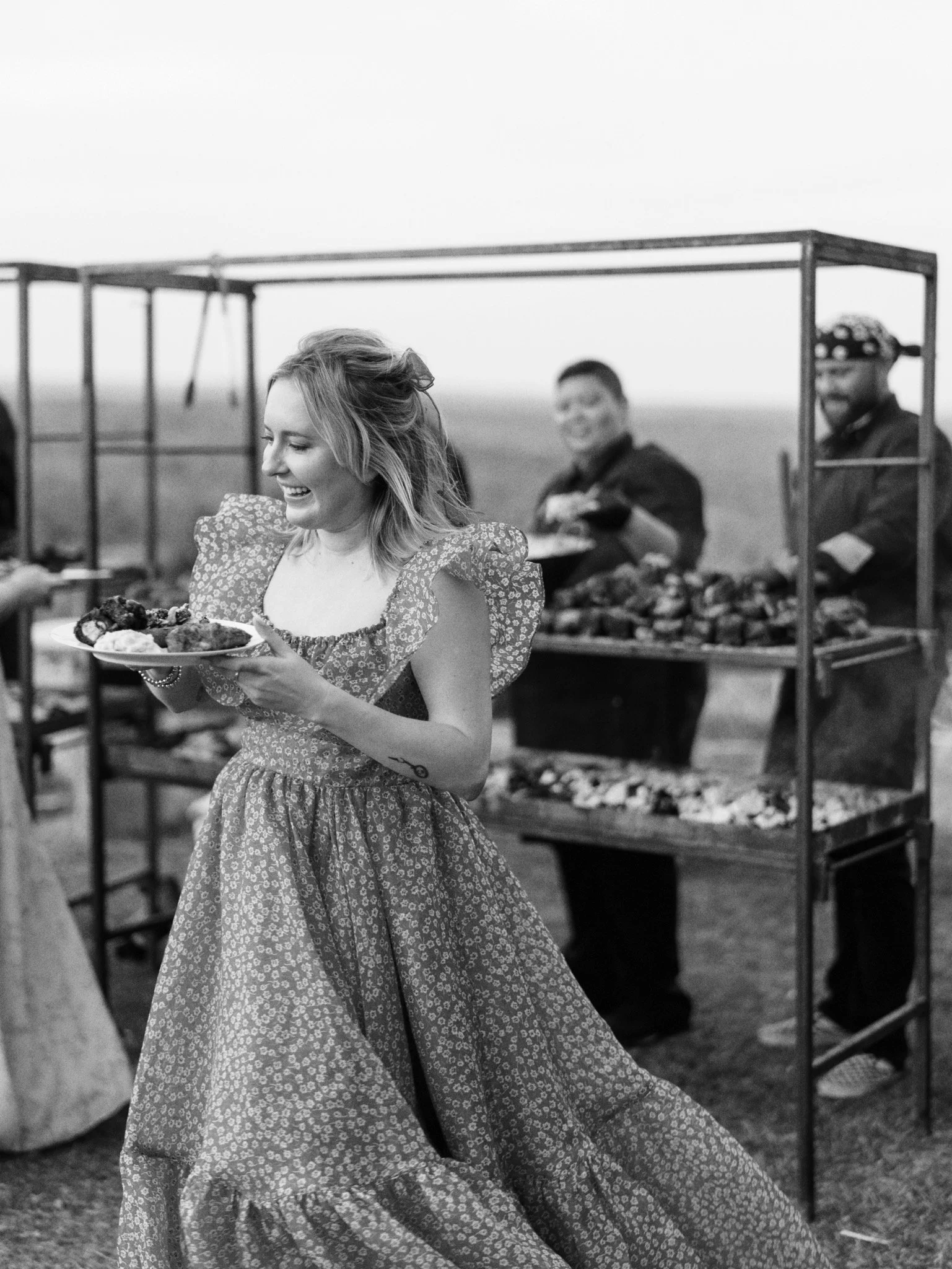 Wedding guest carrying a plate beside Gold Epicure’s live-fire cooking station