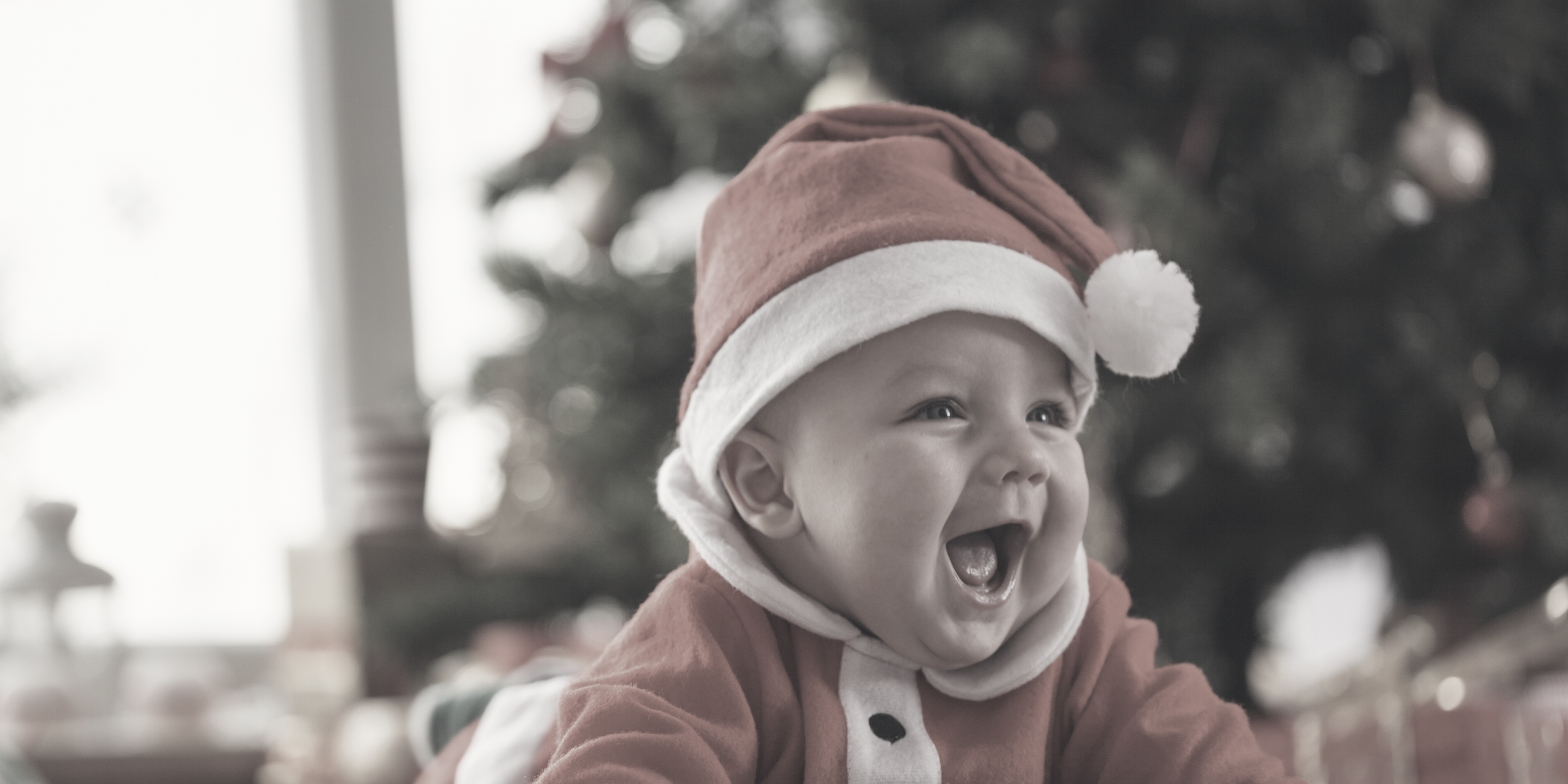 Bebé sonriente vestido de Santa en Navidad, con gorro rojo y blanco, en un ambiente festivo.
