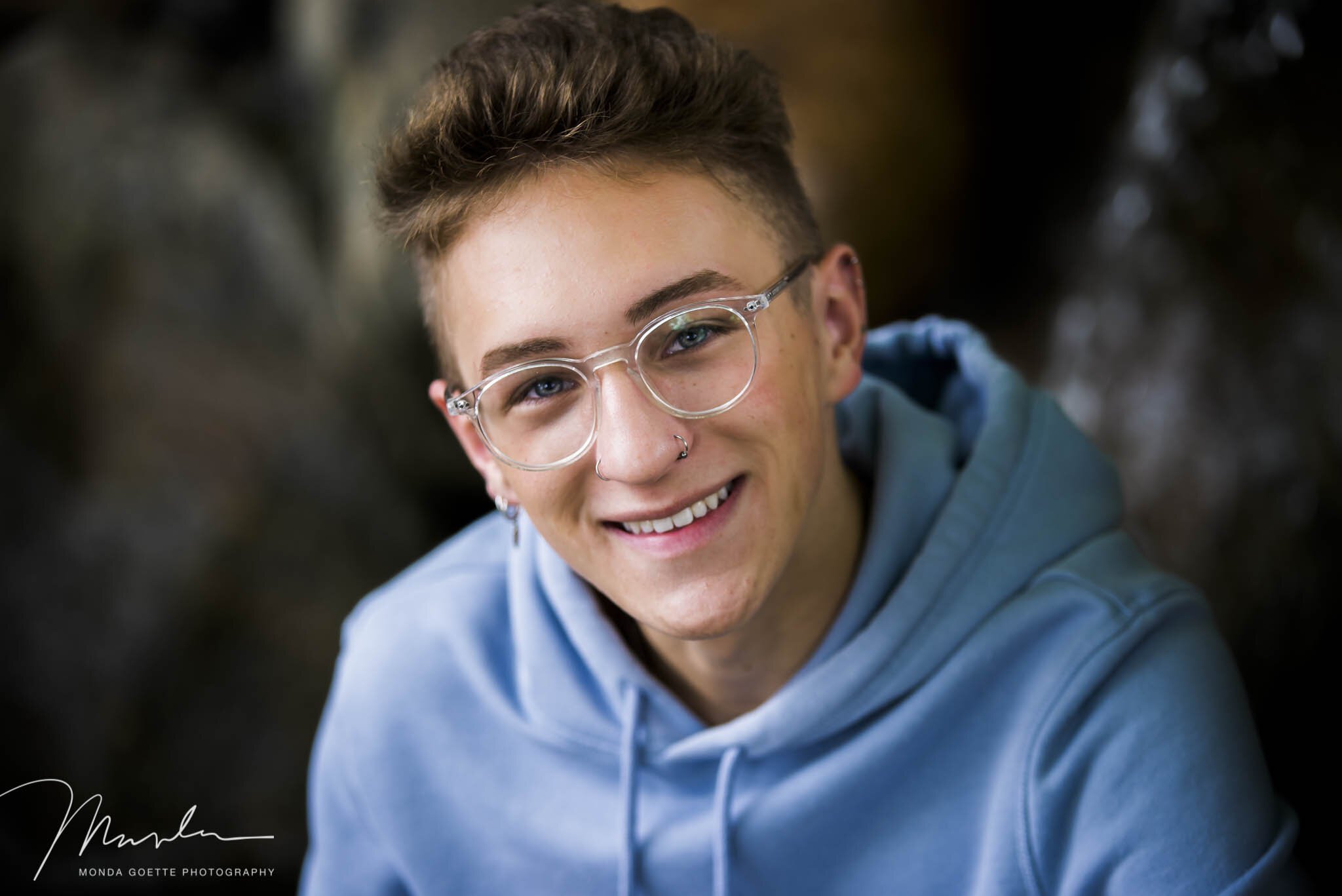 Senior boy with glasses closeup smiling near rocks at photo studio in South St. Paul MN