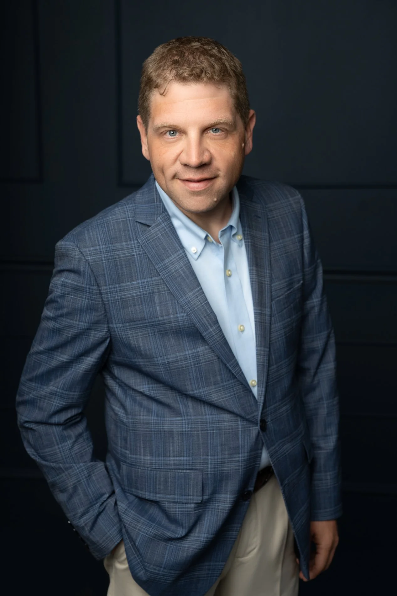 Young adult male poses with hand in pocket on a blue textured backdrop