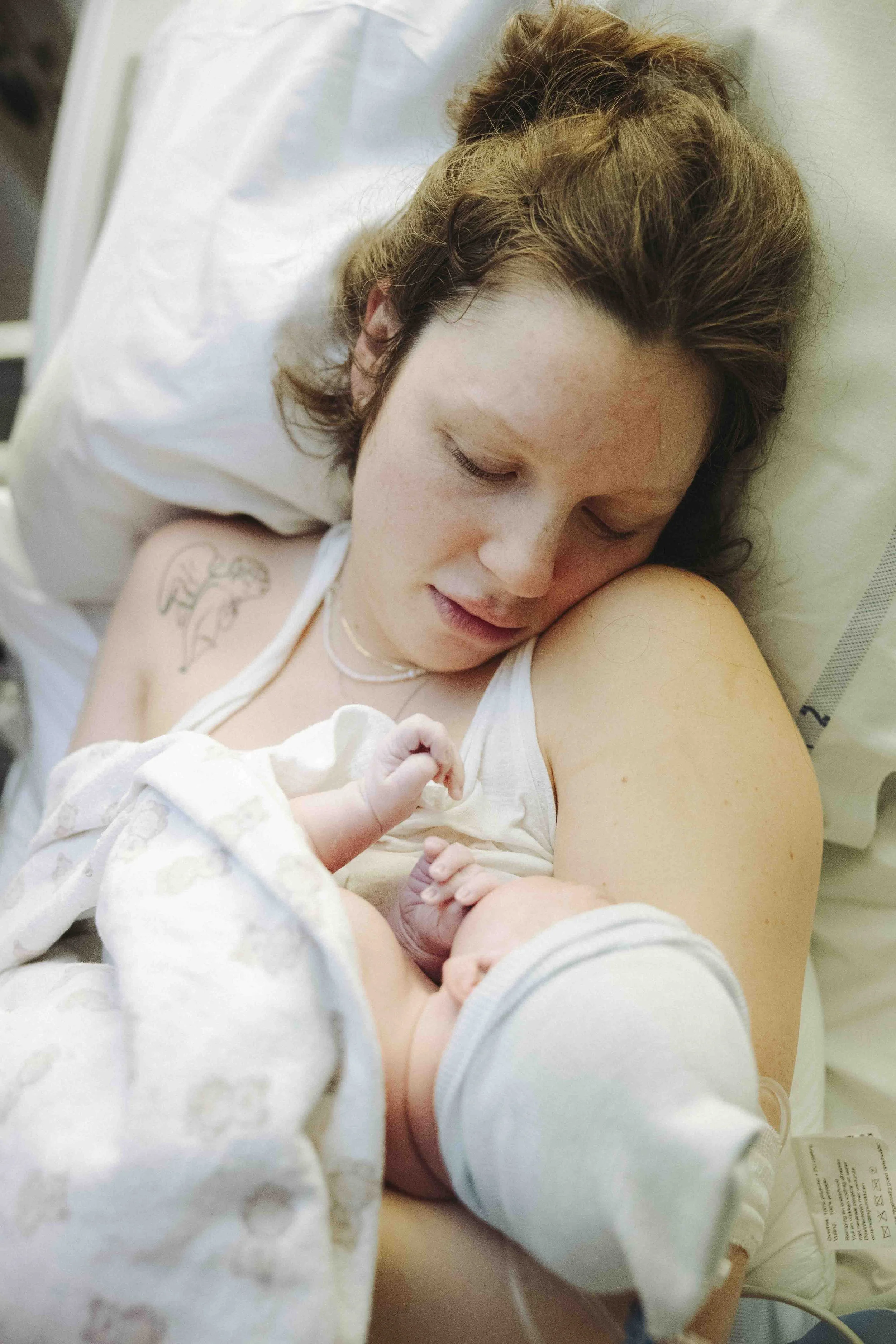 Een vrouw ligt op een ziekenhuisbed en houdt haar pasgeboren baby vast.  Geboortefotografie door Maud Fernhout (de Kraamfotograaf).