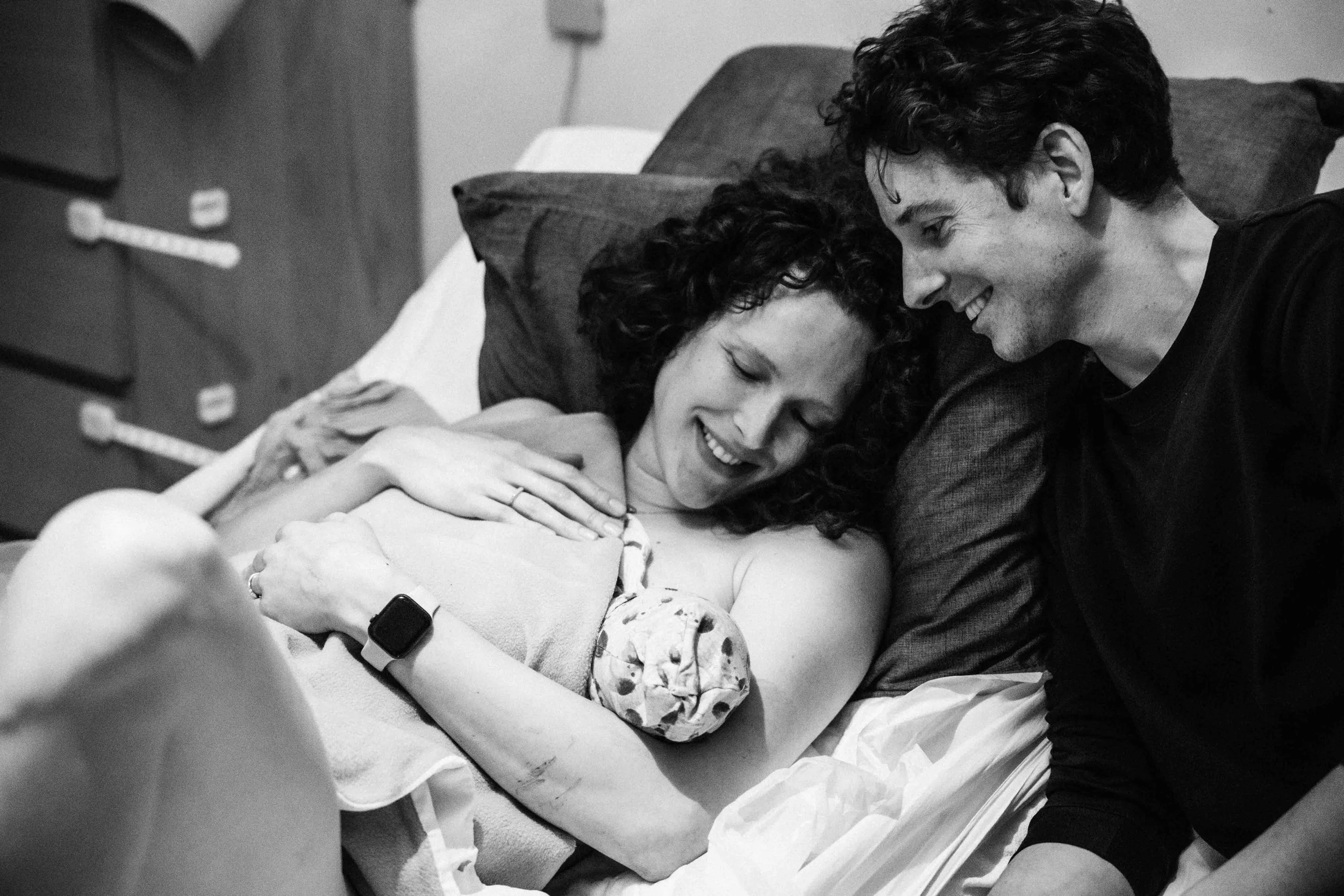 Twee mensen in een ziekenhuis, een persoon ligt in bed en wordt verzorgd door een ander persoon die glimlachend en liefdevol naar haar kijkt.
