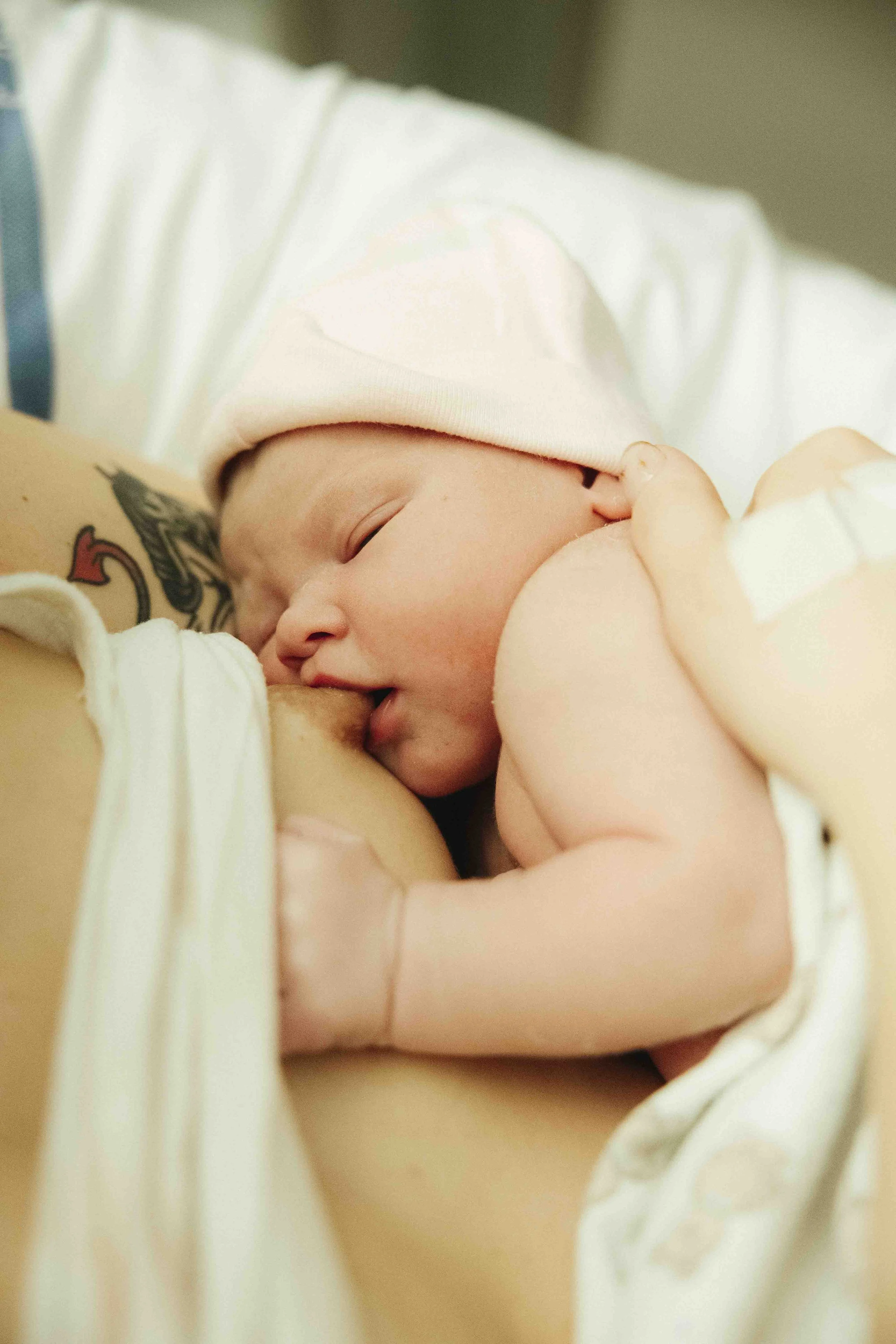 Een pasgeboren baby die drinkt aan de borst van een moeder.  Geboortefotografie door Maud Fernhout (de Kraamfotograaf).