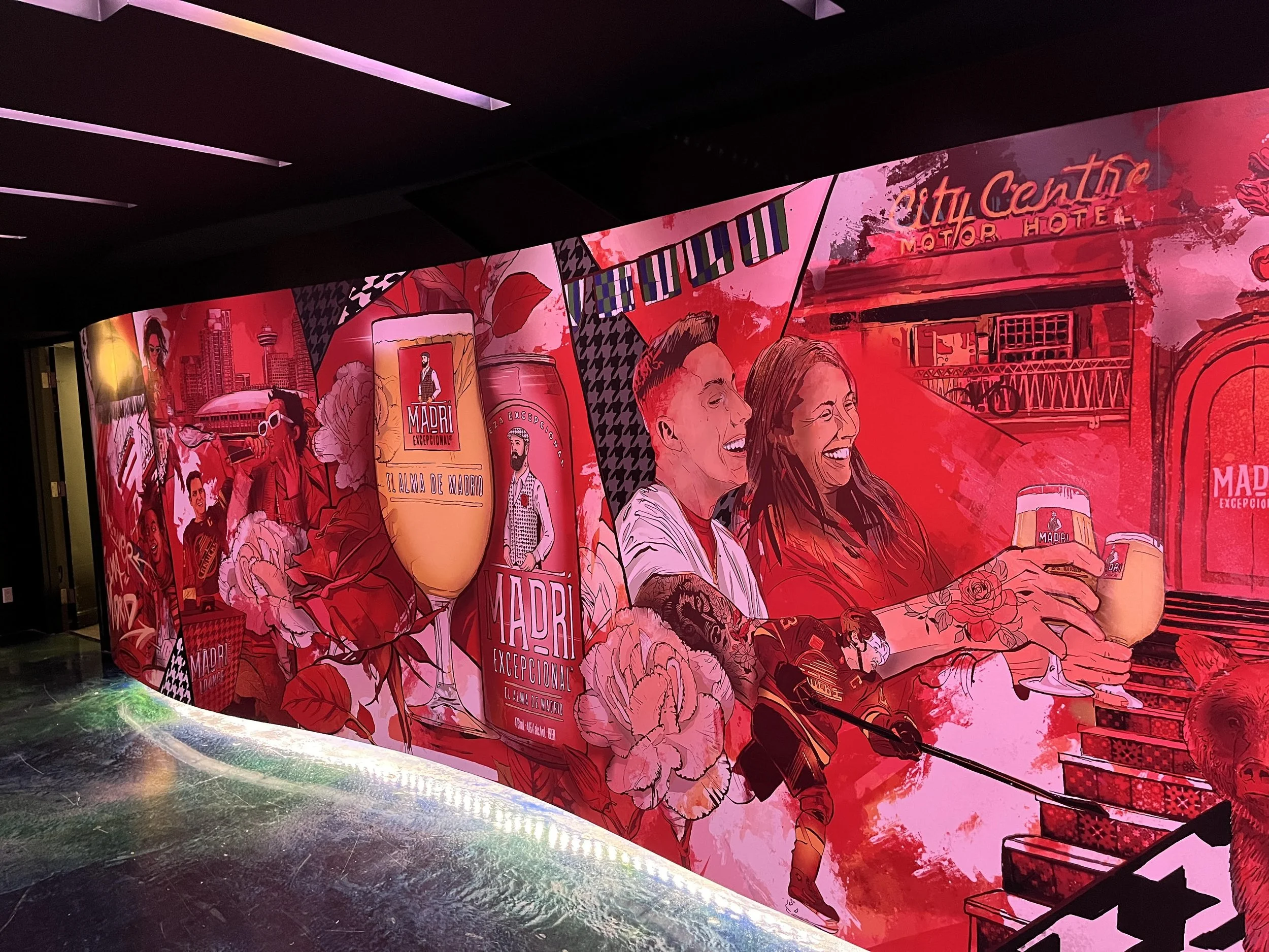 Colorful mural depicting people toasting with drinks, cityscape, and various illustrations, with vibrant reds and pinks, advertising Madrid, Spain.