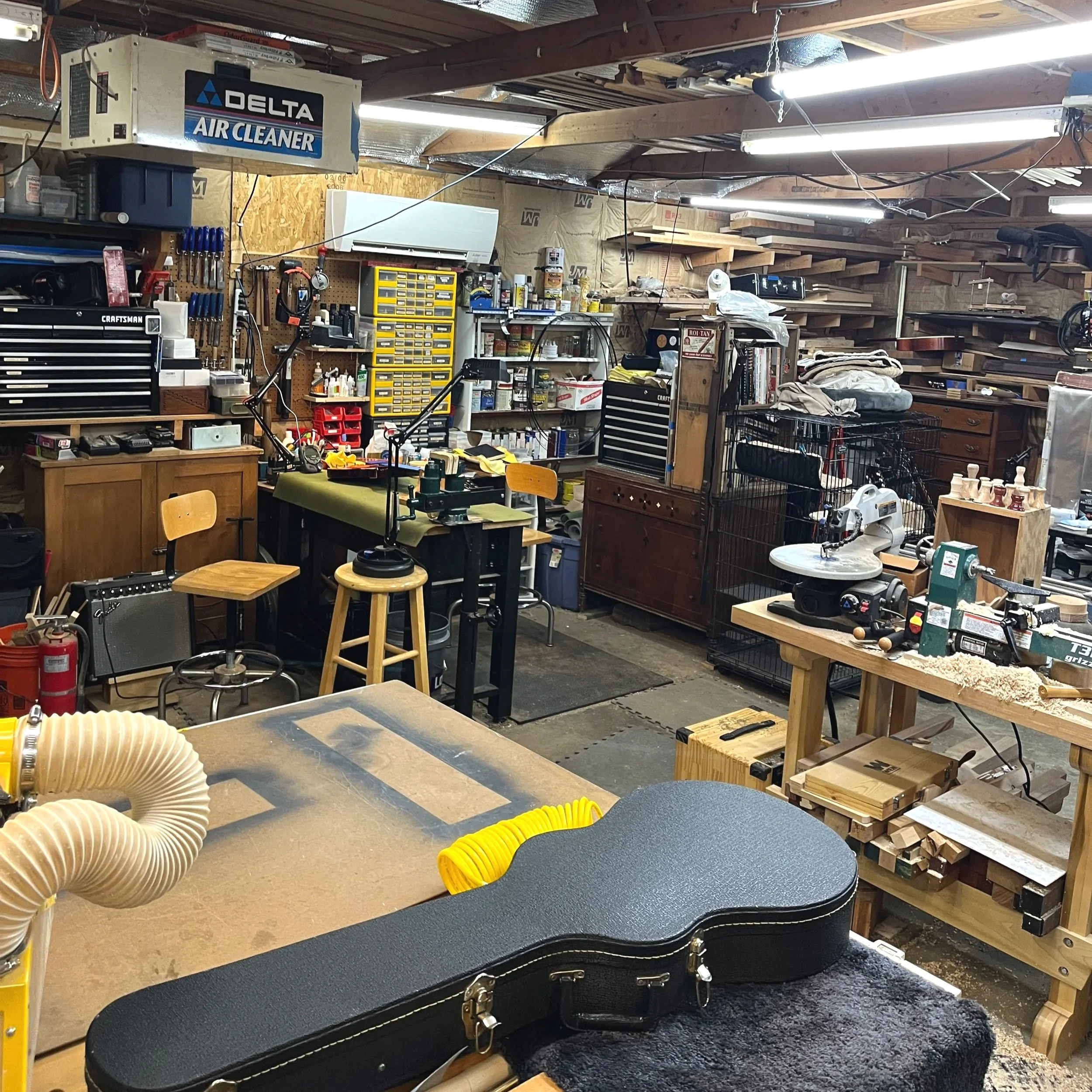 A wide shot of part of the interior of the Two Moons Lutherie workshop with a guitar on the workbench and another on the saw.