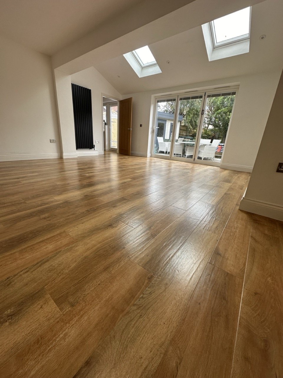 Empty living room with hardwood floors, large glass sliding door, and skylights.