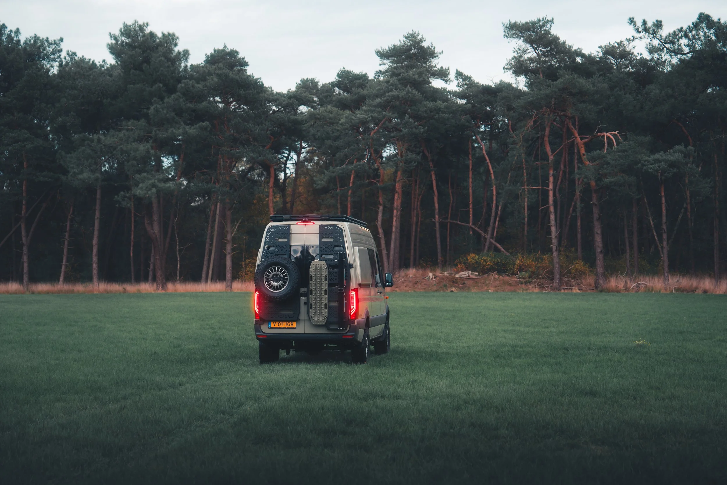 Mercedes Sprinter camping-car roulant sur un champ herbeux en direction d'une forêt de pins