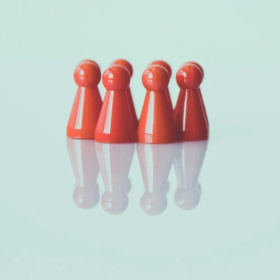 Four red game pieces arranged in a square on a reflective surface with a light blue background.
