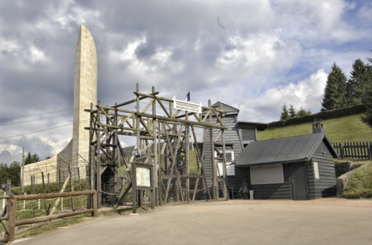 Photo du portail actuel extérieur du camp de Natzweiler, en arrière plan, aperçu du Mémorial national de la déportation © CERD-Struthof.