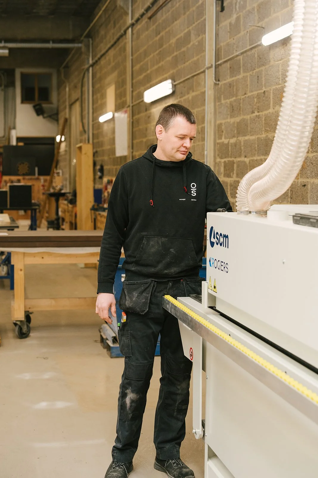 Man in een roze hoodie die naar de camera kijkt en op een lichte achtergrond staat.