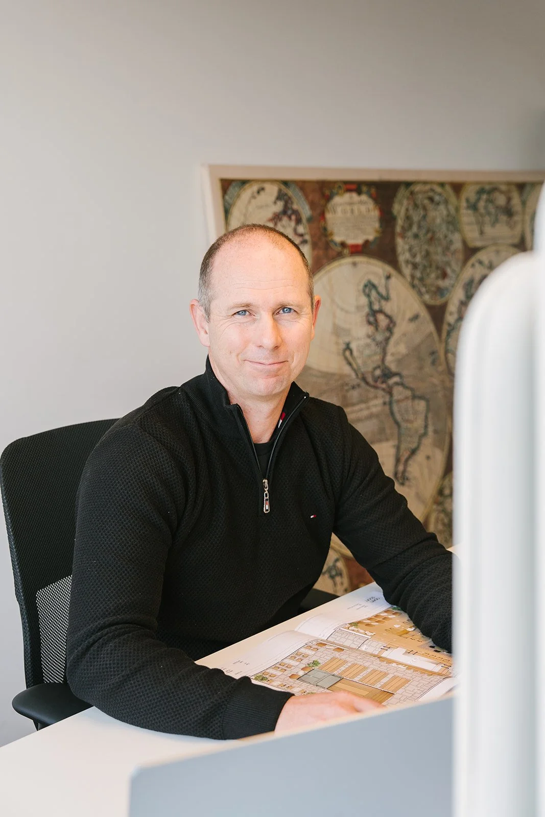 Portret van een man met kort haar die met gekruiste armen naar de camera kijkt, tegen een lichte achtergrond.