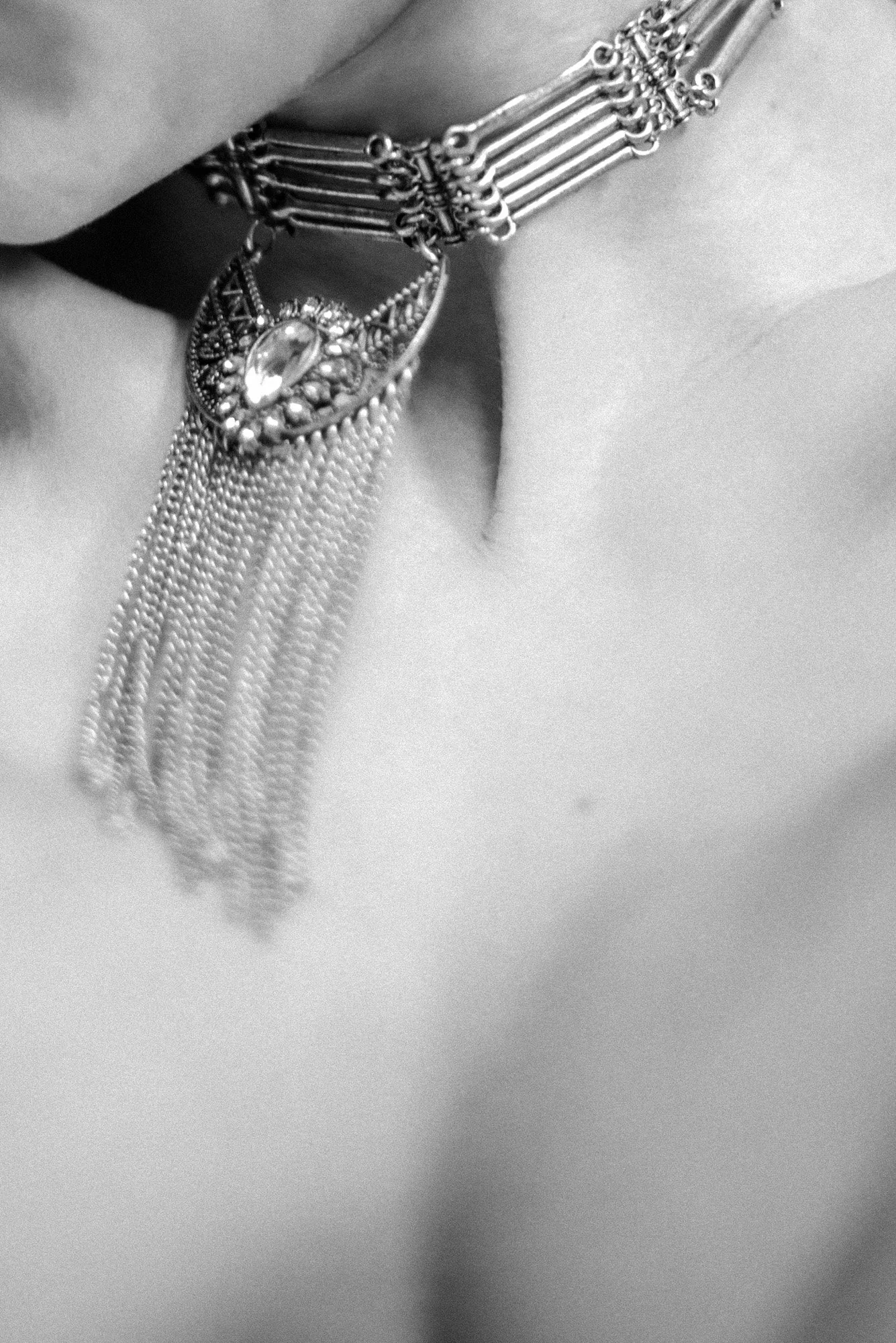 Abstract black-and-white close-up of collarbone and statement necklace with soft motion blur.