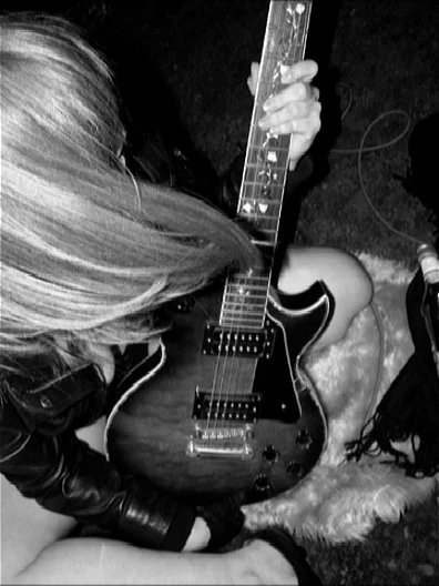 black and white self-portrait of a woman wearing a leather jacket, sitting on a roof top holding a guitar