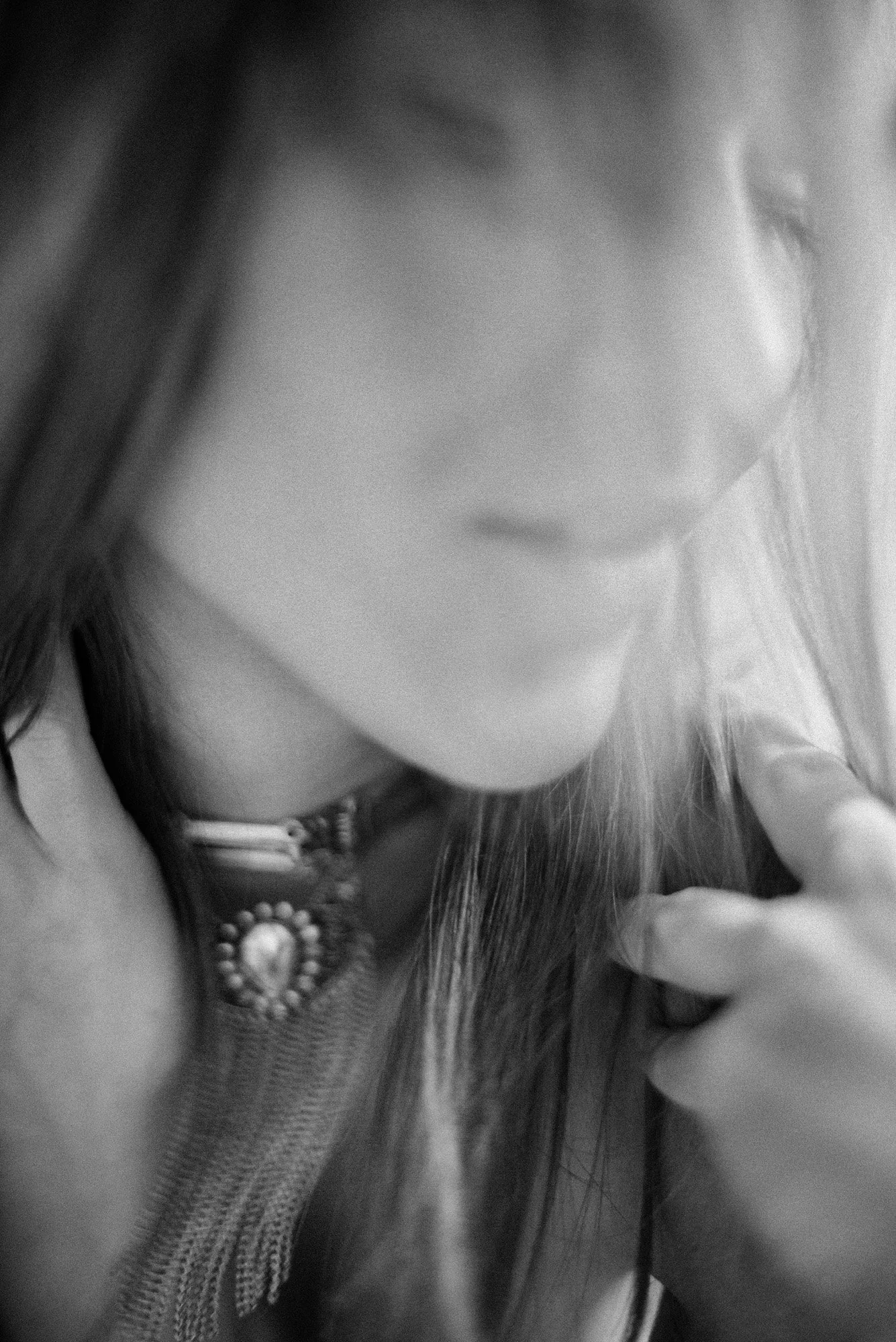 Blurred black-and-white close-up portrait with soft motion, partially obscured face and flowing hair.