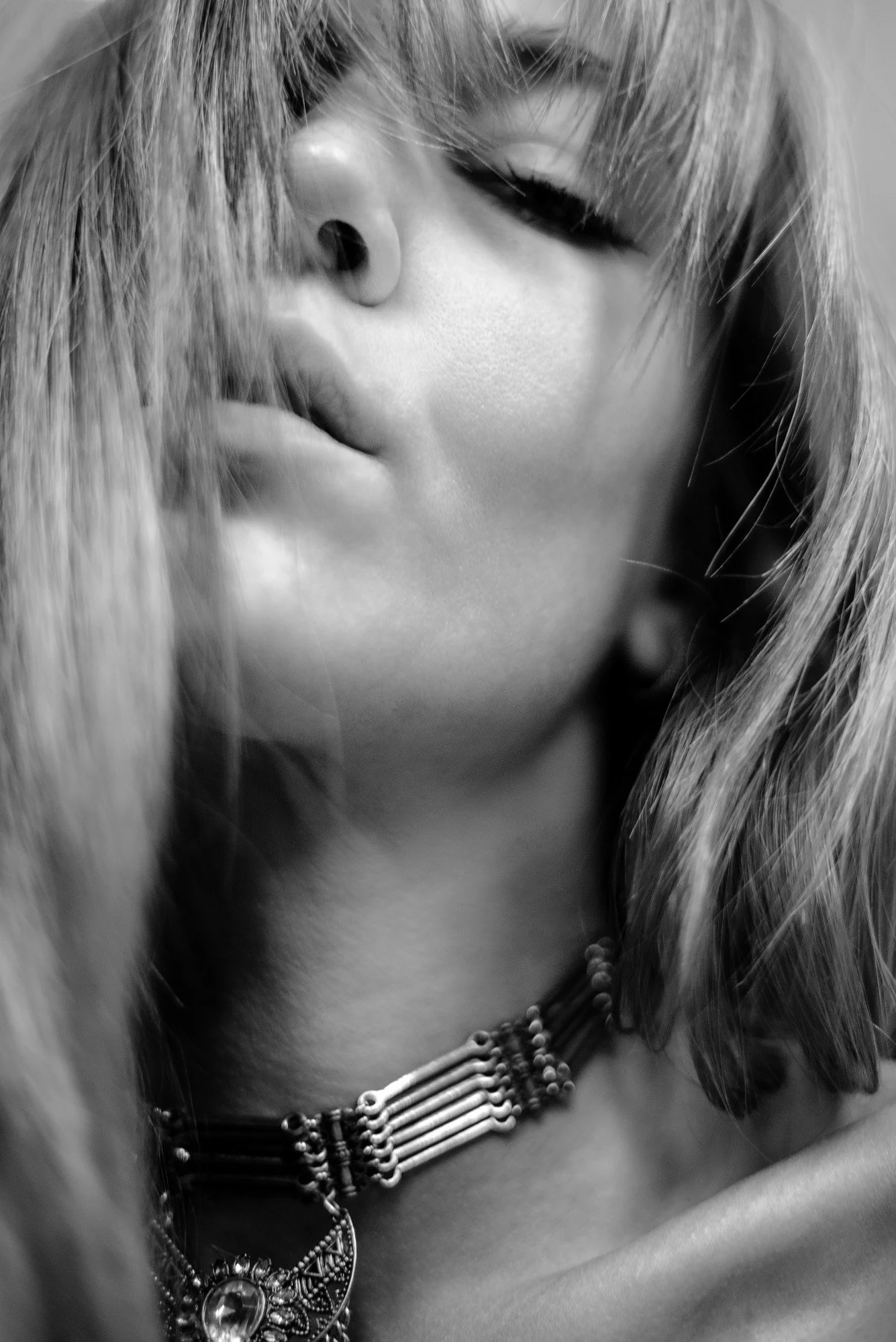 black-and-white close-up portrait with necklace in soft motion, partially obscured face and flowing hair.