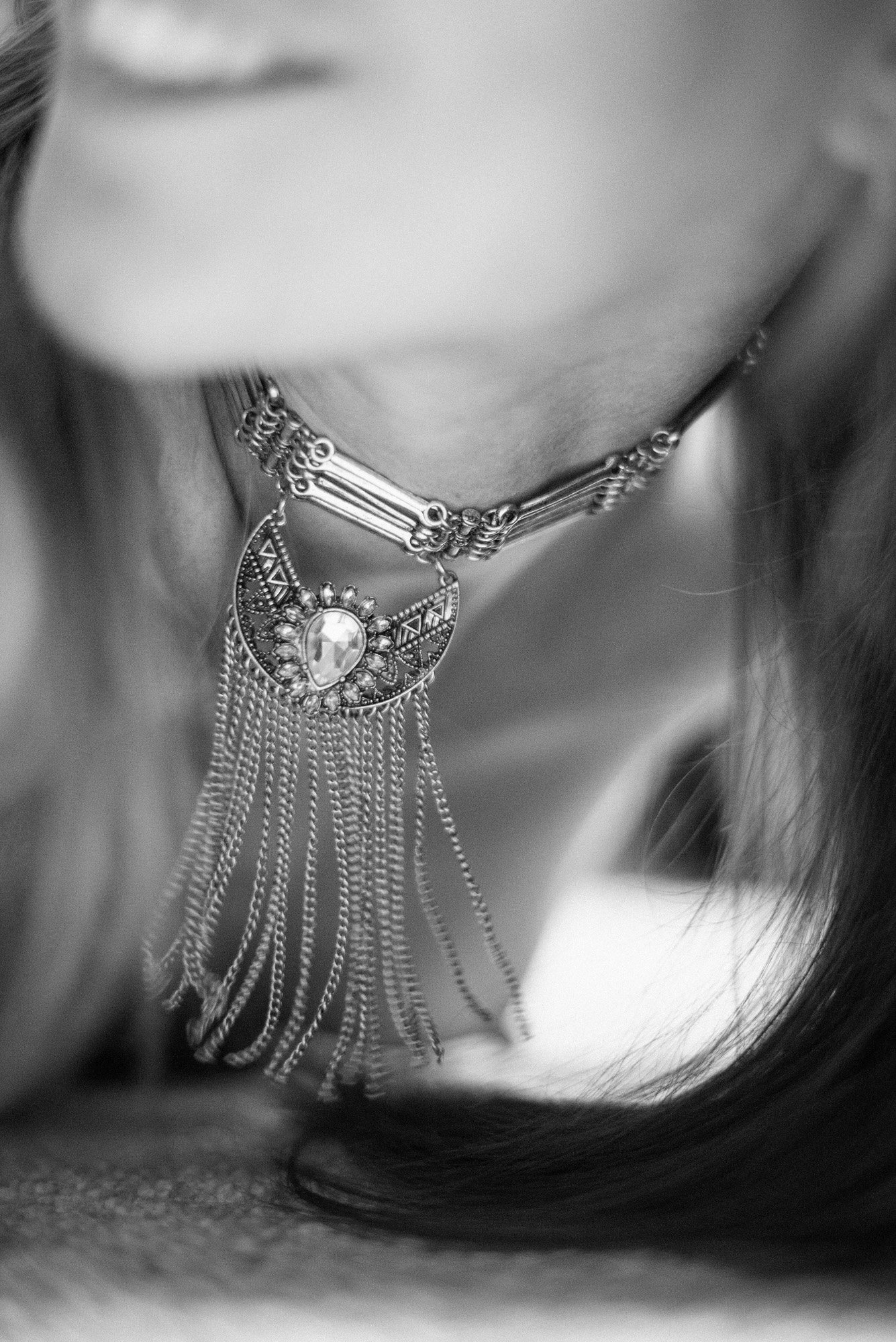 Minimal black-and-white portrait fragment with statement necklace showing a soft smile in shallow focus.