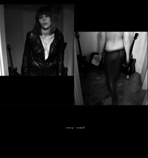 Black and white self-portrait showing a woman standing indoors in a leather jacket, with a guitar visible in the background.