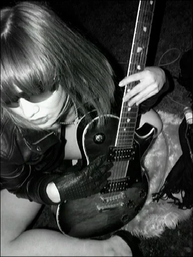 black and white self-portrait of a woman wearing a leather jacket, sun glasses, sitting on a roof top holding a guitar