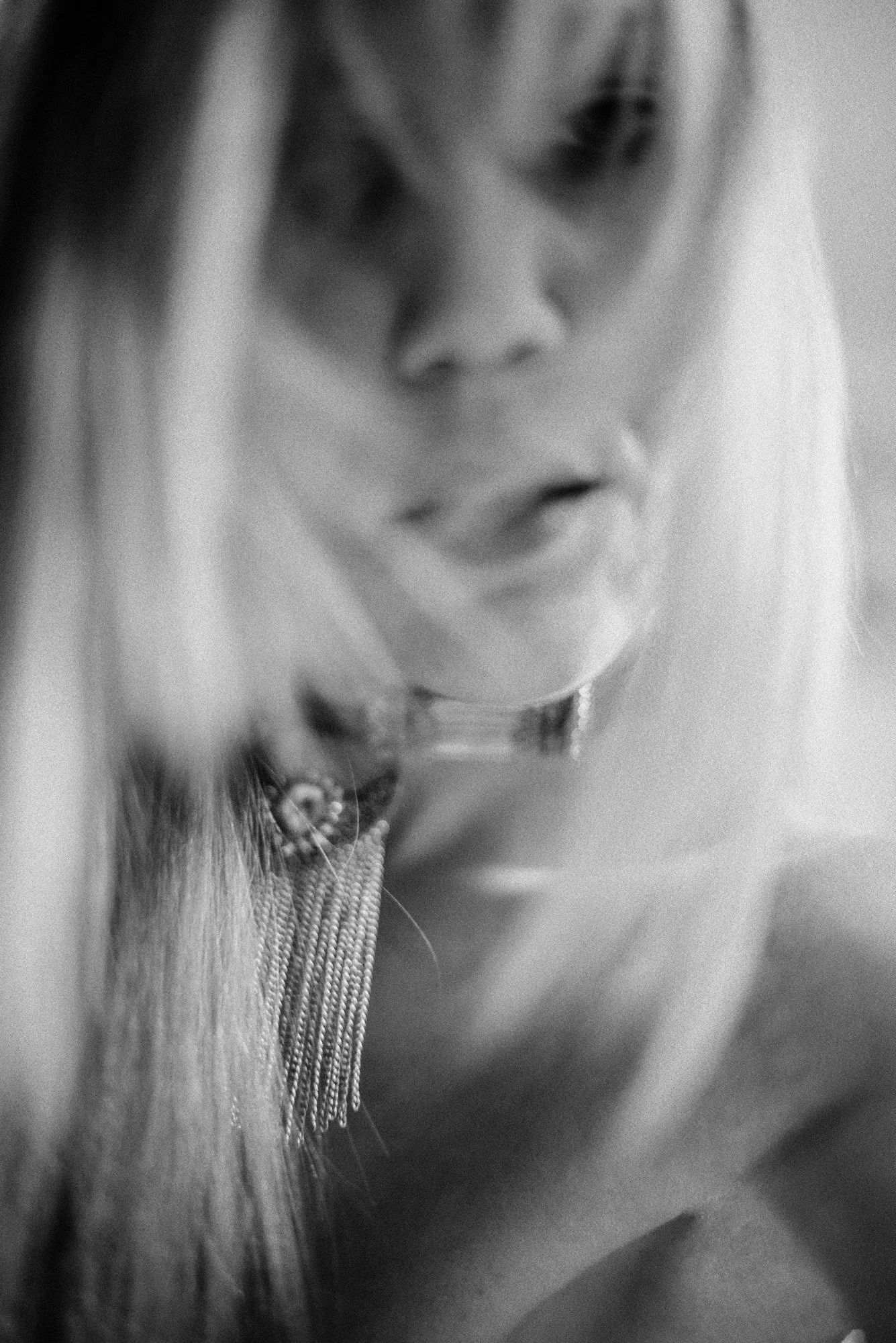 Blurred black-and-white close-up portrait with soft motion, partially obscured face and flowing hair.