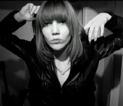 Color self-portrait of a woman with straight bangs covering her eyes, wearing a leather jacket, photographed indoors.