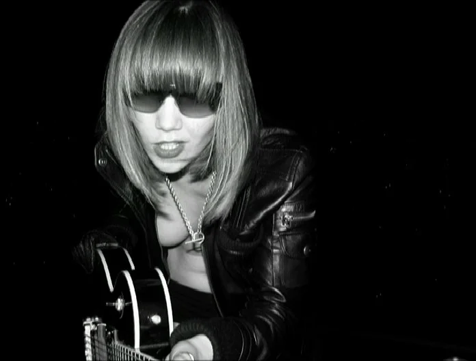 Black and white self-portrait at night showing a woman in a leather jacket leaning forward with an electric guitar, photographed on a rooftop.