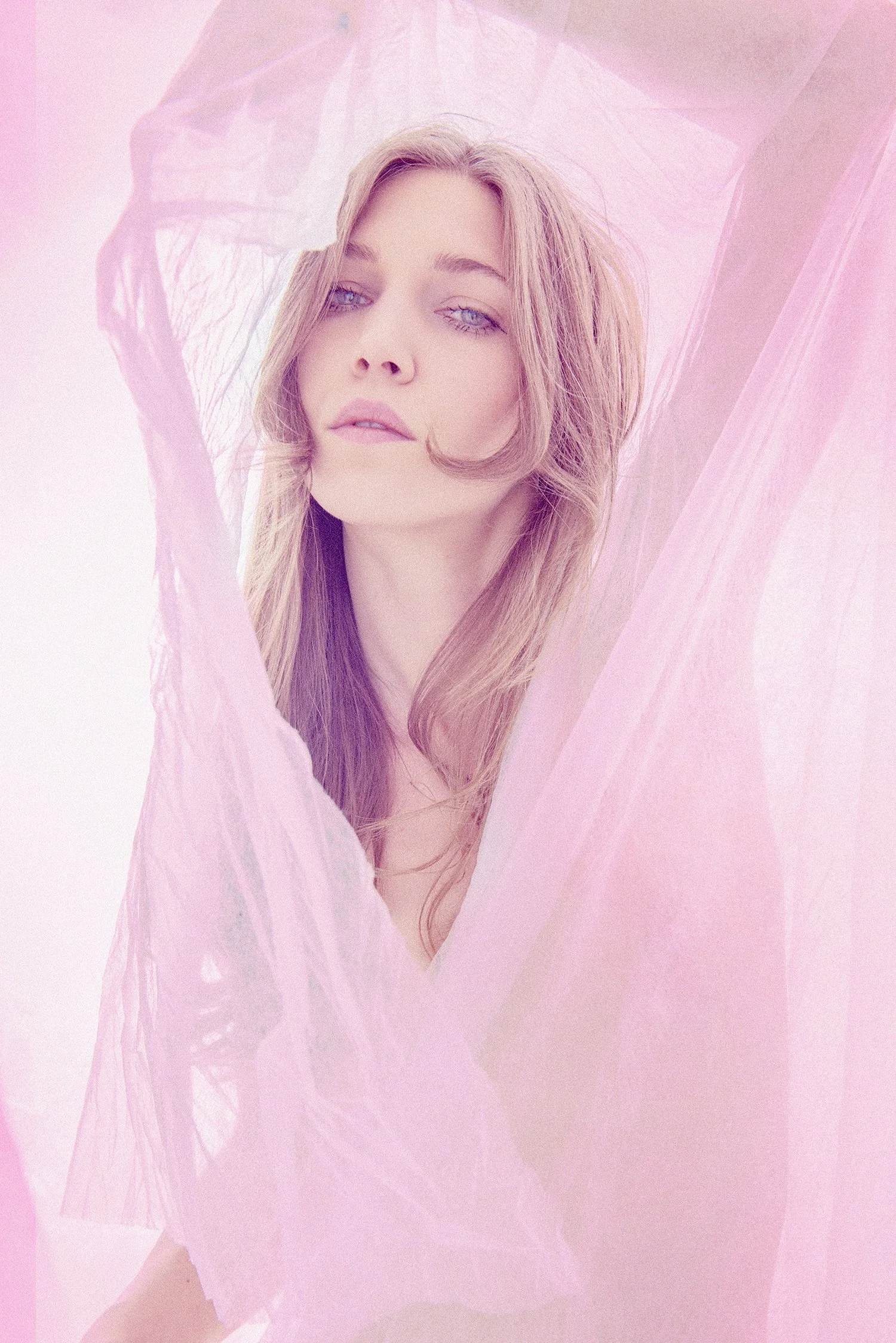 Ethereal self-portrait framed by translucent fabric, capturing softness, presence, and emotional truth in pastel light.