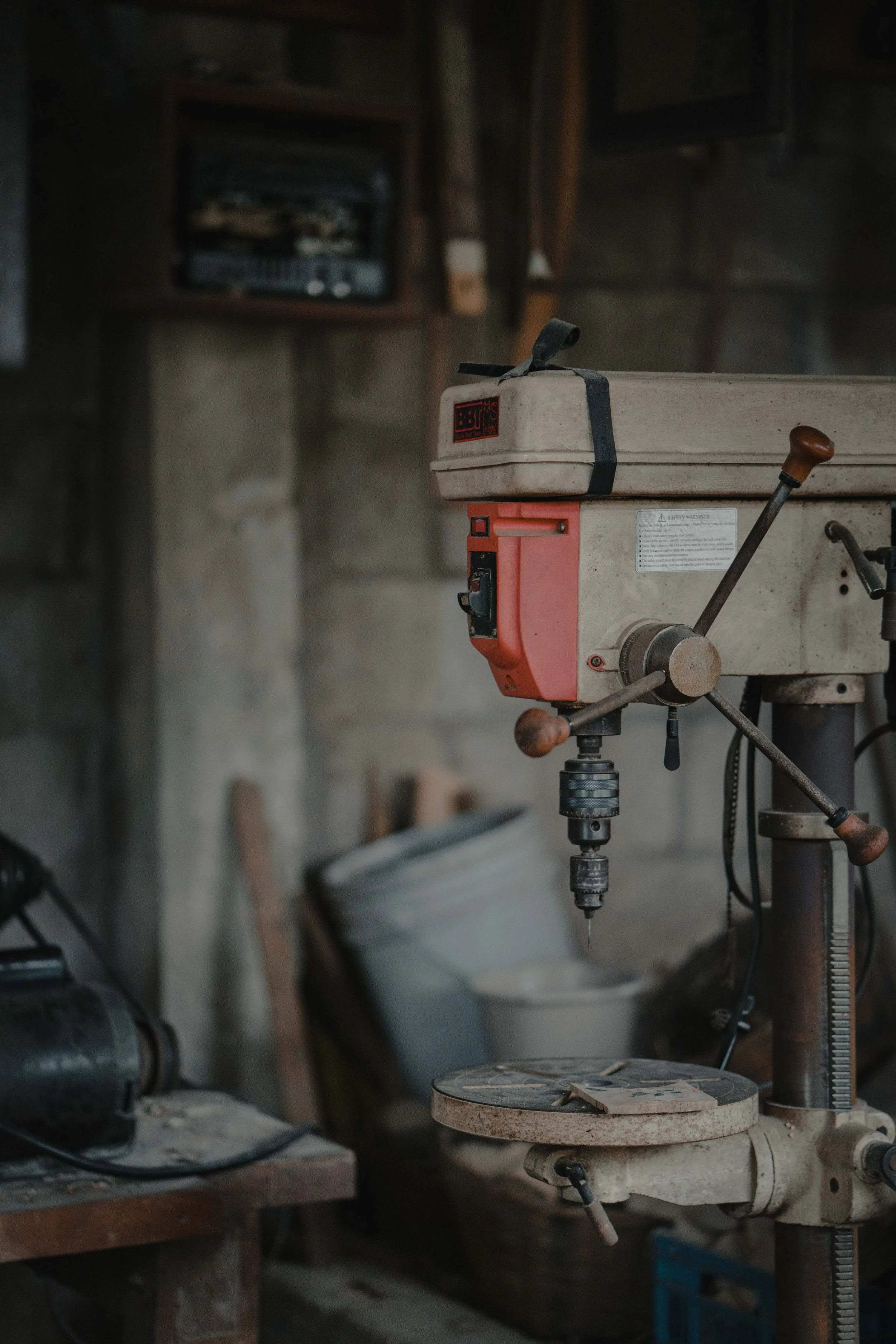 Vintage industrial drill press in a workshop setting with tools and equipment.