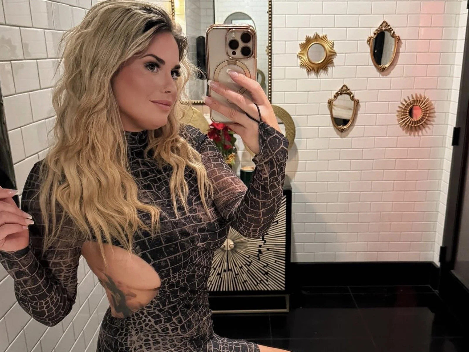 Abby Rose posing for a mirror selfie in a dark patterned dress
