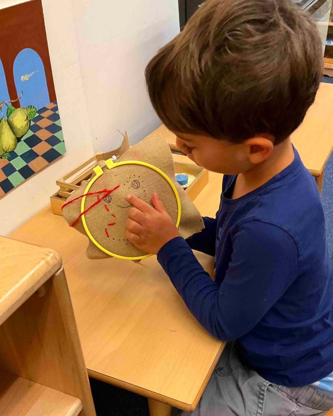 This child is sewing a frog. The dots on the cloth guide his placement of the needle. The dots are intentionally close together to encourage making small stitches in order to create a defined shape. With practice the child will be able to sew an outl