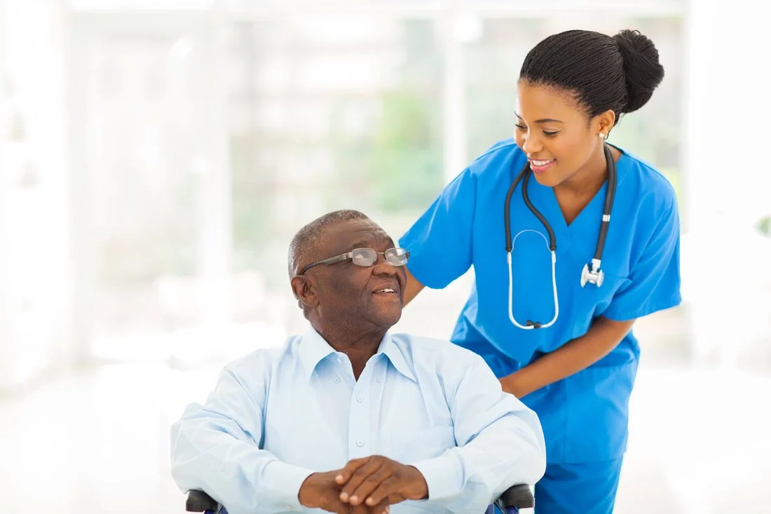 Elderly man in wheelchair looking at nurse that is pushing him