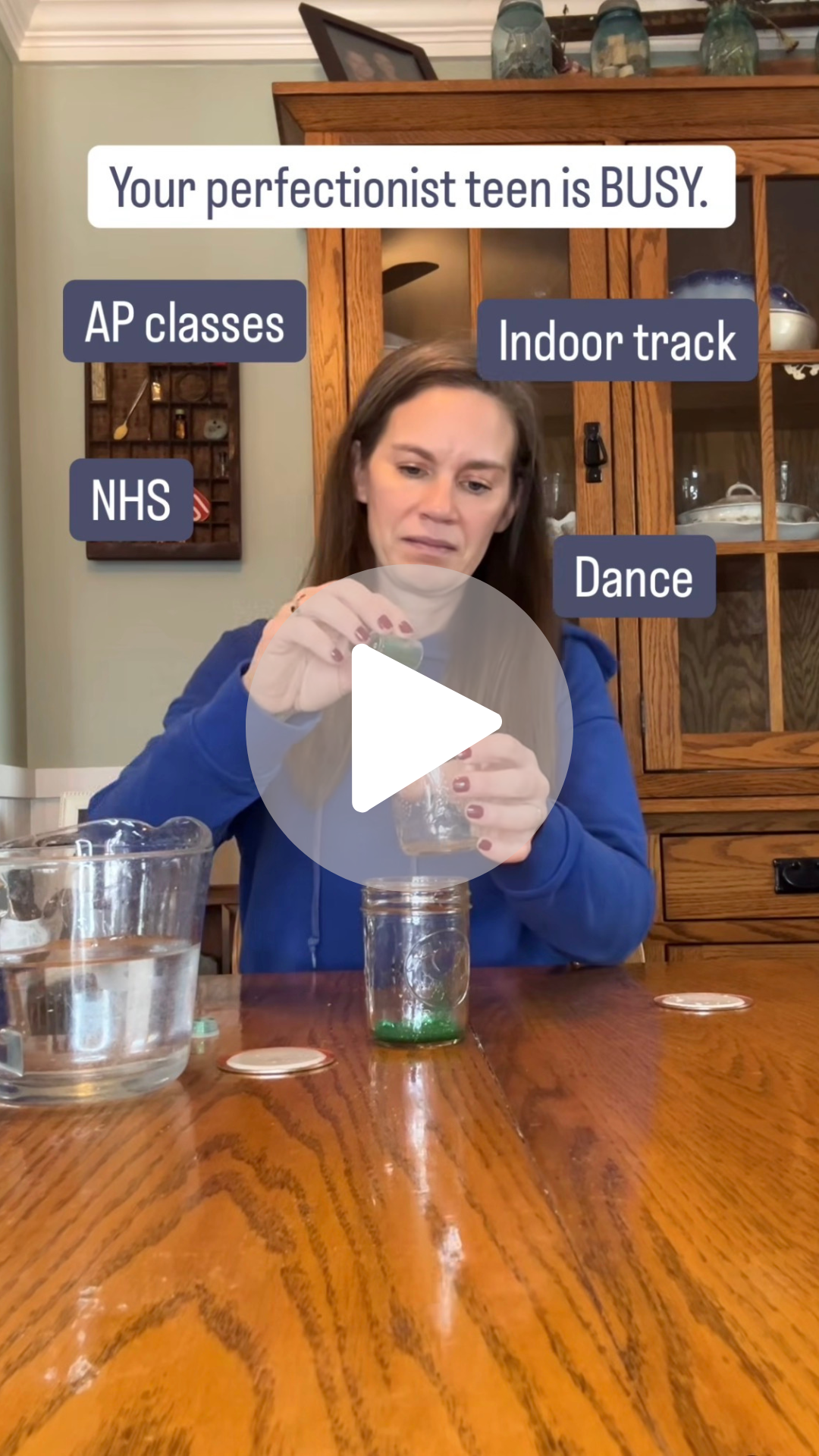 Woman with brown hair and blue sweatshirt sitting at a table putting glitter and water in a jar